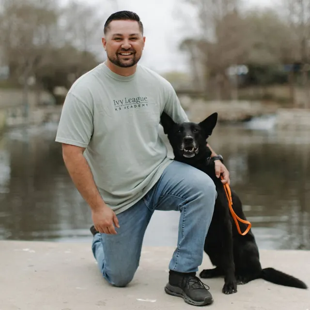 Ivy League Canine Academy trainer kneeling beside a black shepherd on the San Antonio River Walk
